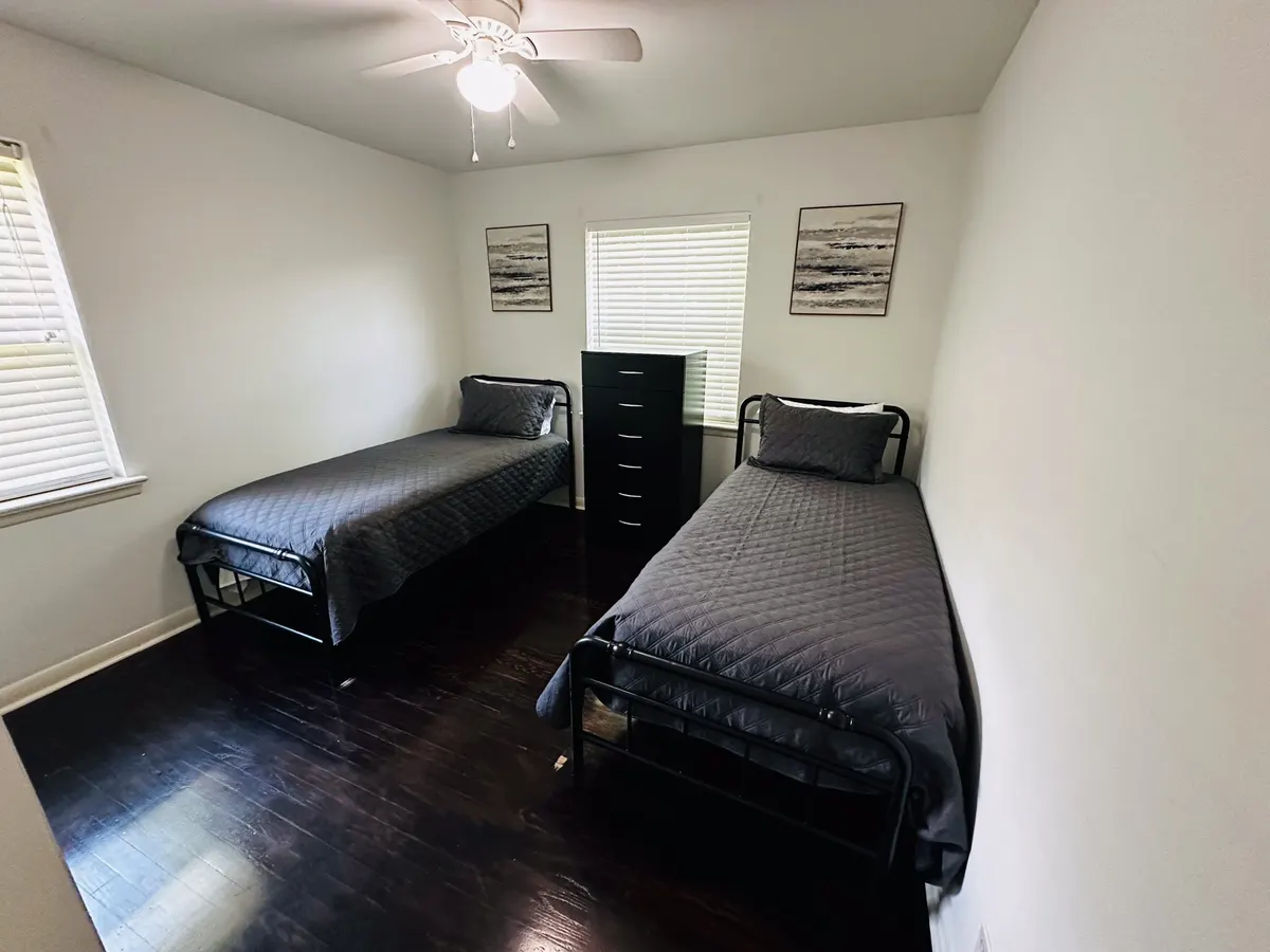 A second shared bedroom with two single beds, a dresser and framed prints in an Austin sober living home
