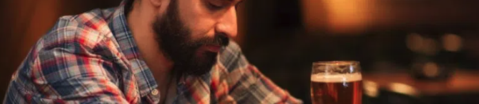 Man sitting alone with a glass of beer, reflecting the struggle of alcohol addiction.