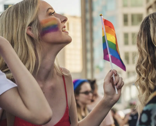 Woman celebrating Pride Month in Austin with rainbow face paint and flag at a sober community event.