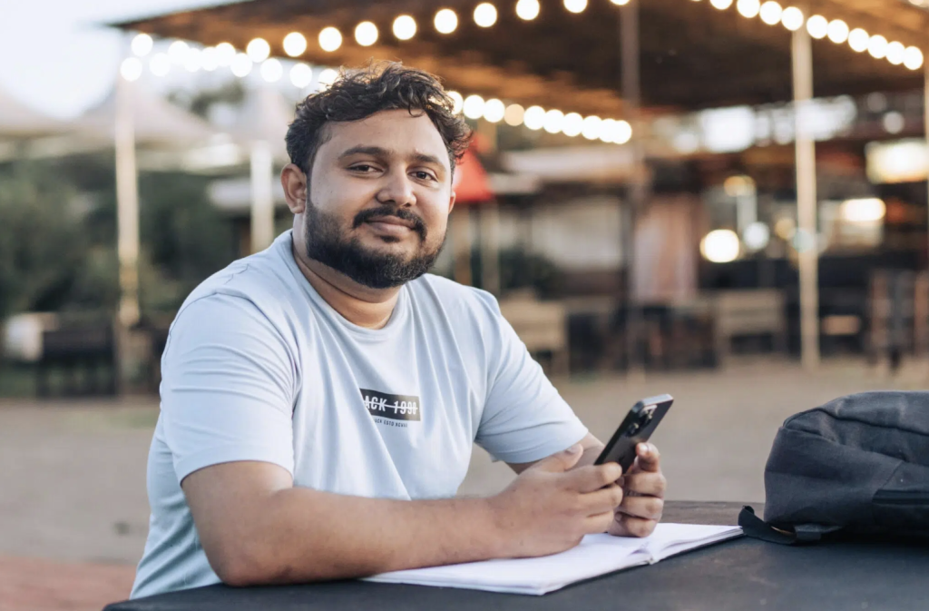 A man seated outdoors with a notebook and smartphone, representing an individual considering rehab options and evaluating treatment plans.