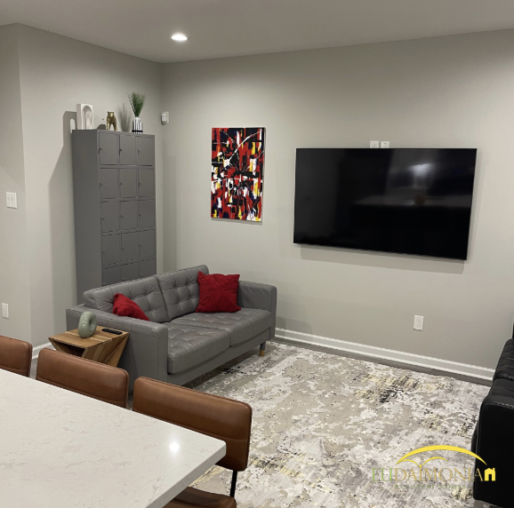 Community lounge with sofa, lockers, large TV, and artwork in a Houston sober living home.