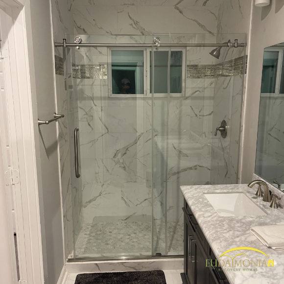 Updated bathroom with glass walk-in shower and marble tile in a Houston sober living home.