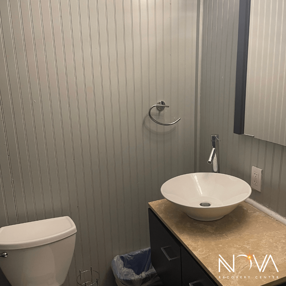 Bathroom with vessel sink, toilet, and beadboard walls at Nova Recovery Center in Austin.