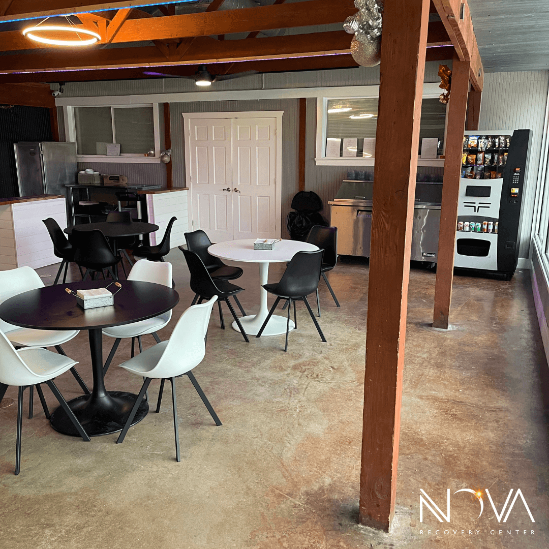 Communal dining room with round tables, mixed seating, vending, and a kitchen counter at Nova Recovery Center.