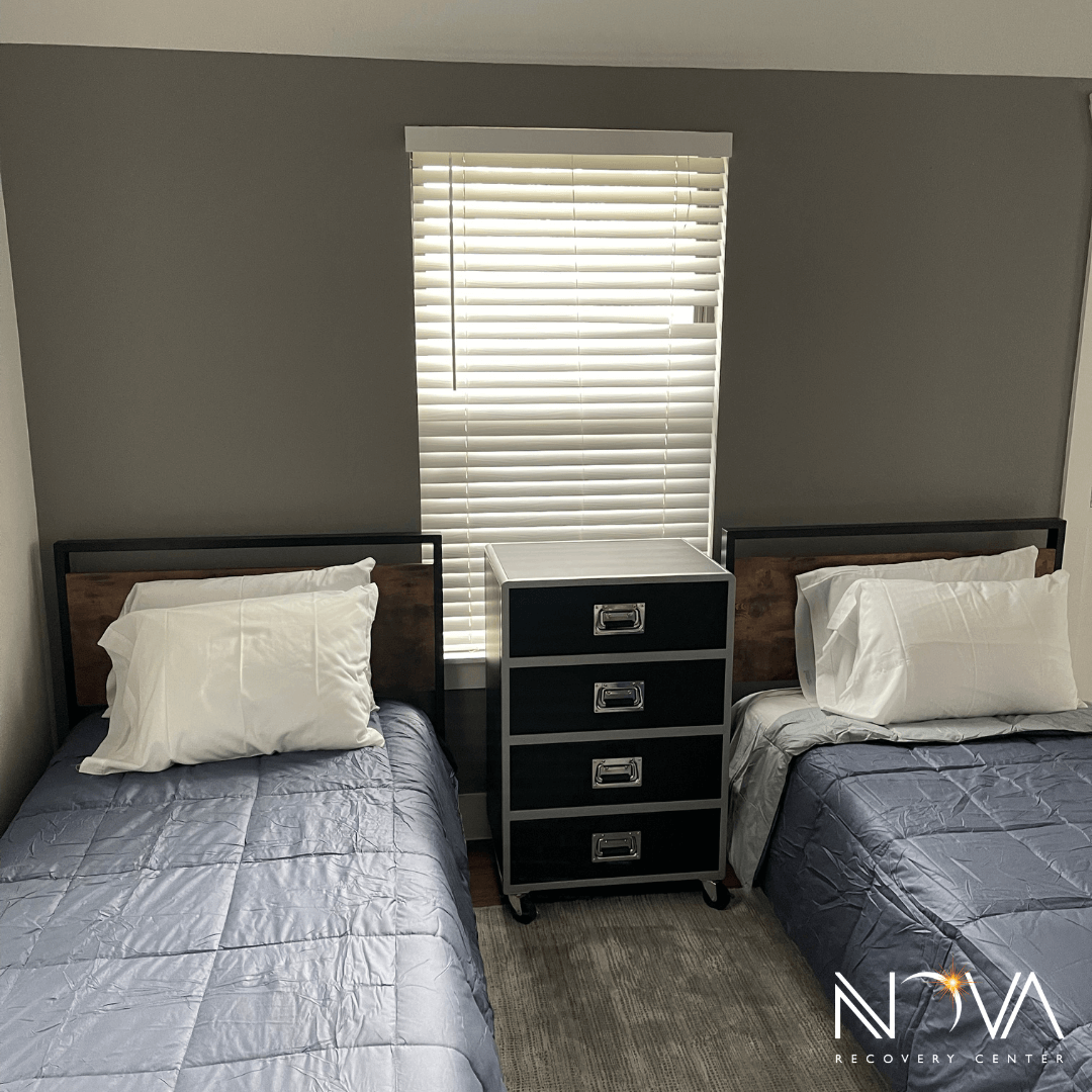 Double‑occupancy bedroom with two twin beds and a shared chest beneath a window at Nova Recovery Center.