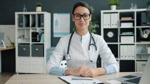 A female doctor wearing a stethoscope sits at her desk. -- Photo by Vitaly Gariev on Unsplash