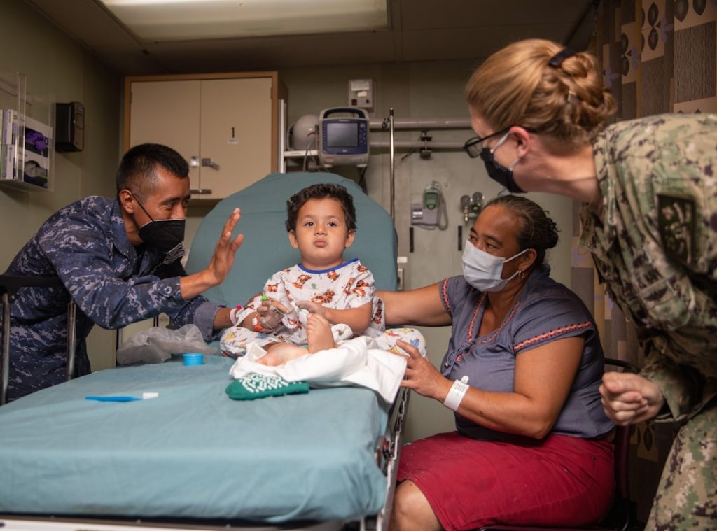 A child sits on a medical bed with adults around. -- Photo by Navy Medicine on Unsplash