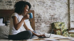 Woman drinking coffee while using laptop in bed. -- Photo by Vitaly Gariev on Unsplash